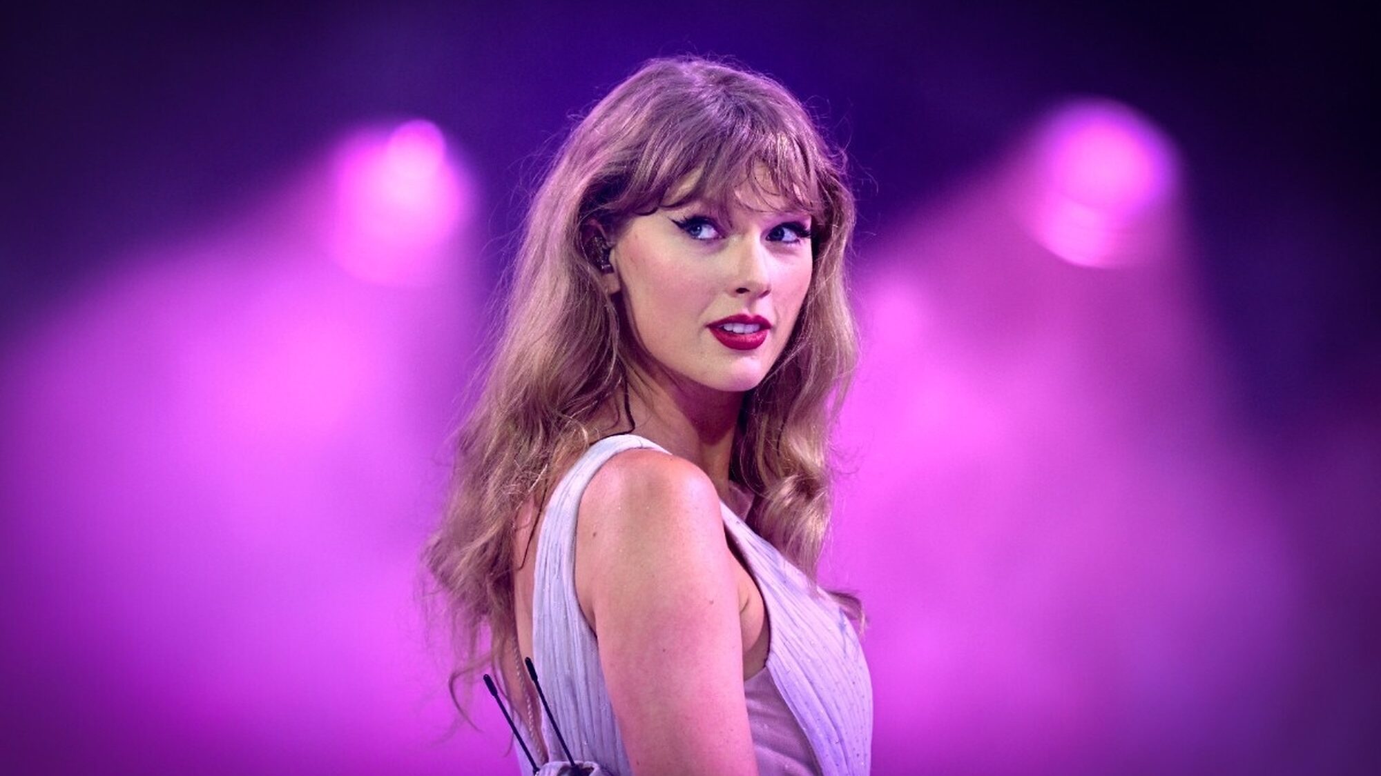 Blonde Amerikaanse zangeres Taylor Swift kijkt zwoel naar de camera met een roze achtergrond.