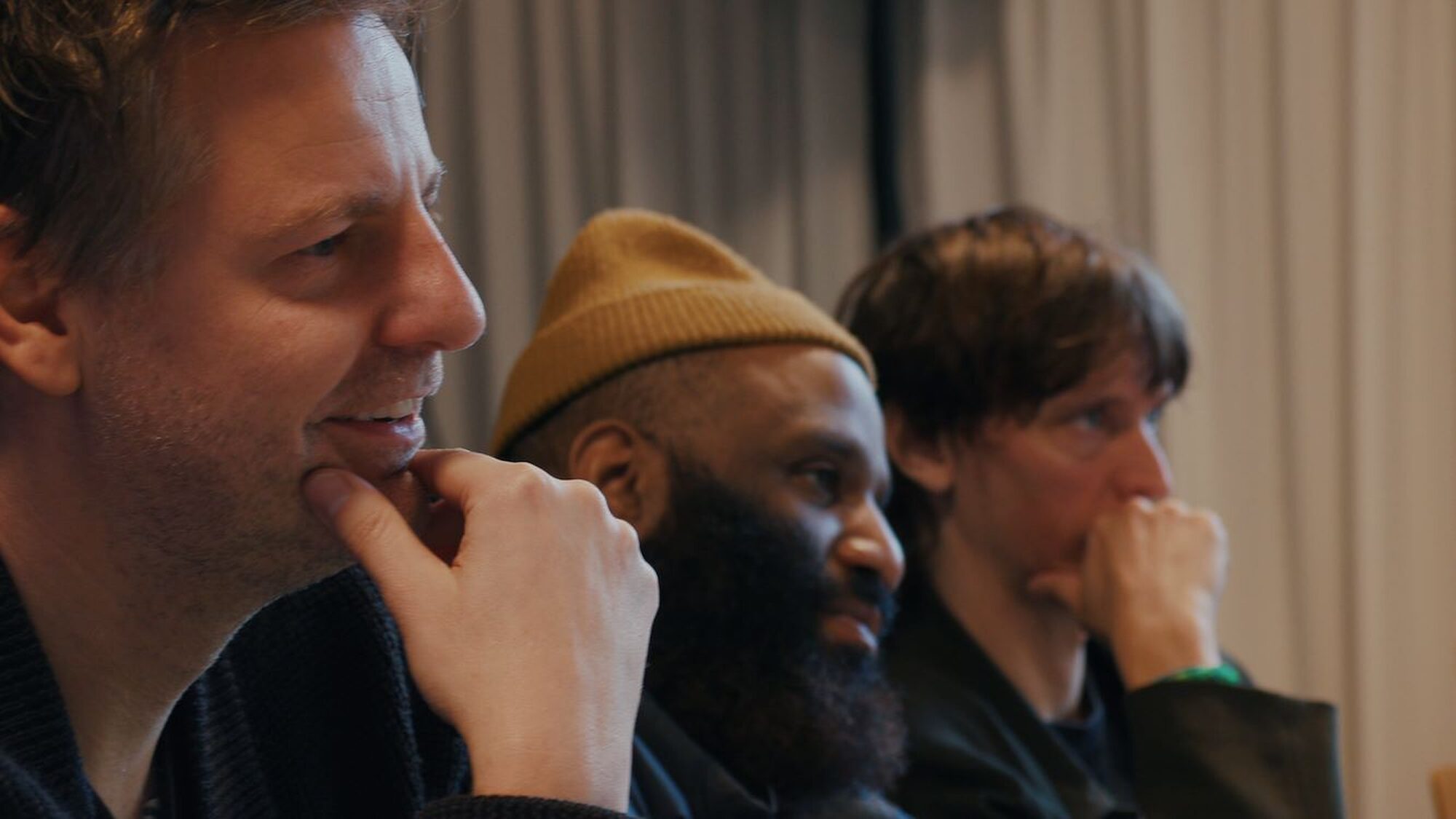 De drie mannen van de jeugd van tegenwoordig zitten bedenkelijk te kijken aan een tafel naar audities