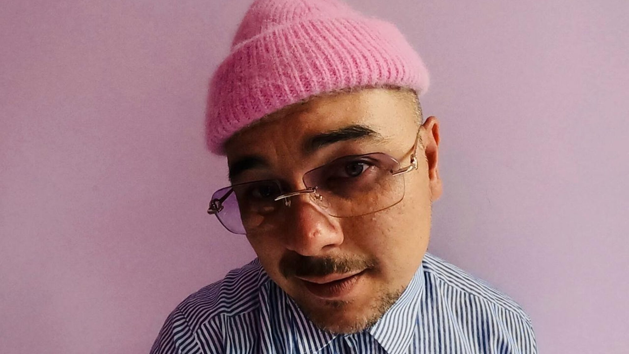 Een foto van (radio) DJ Justin Verkijk. Hij staat voor een roze achtergrond en heeft een roze muts op. Hij houdt zijn hoofd een beetje scheef en kijkt de camera in.