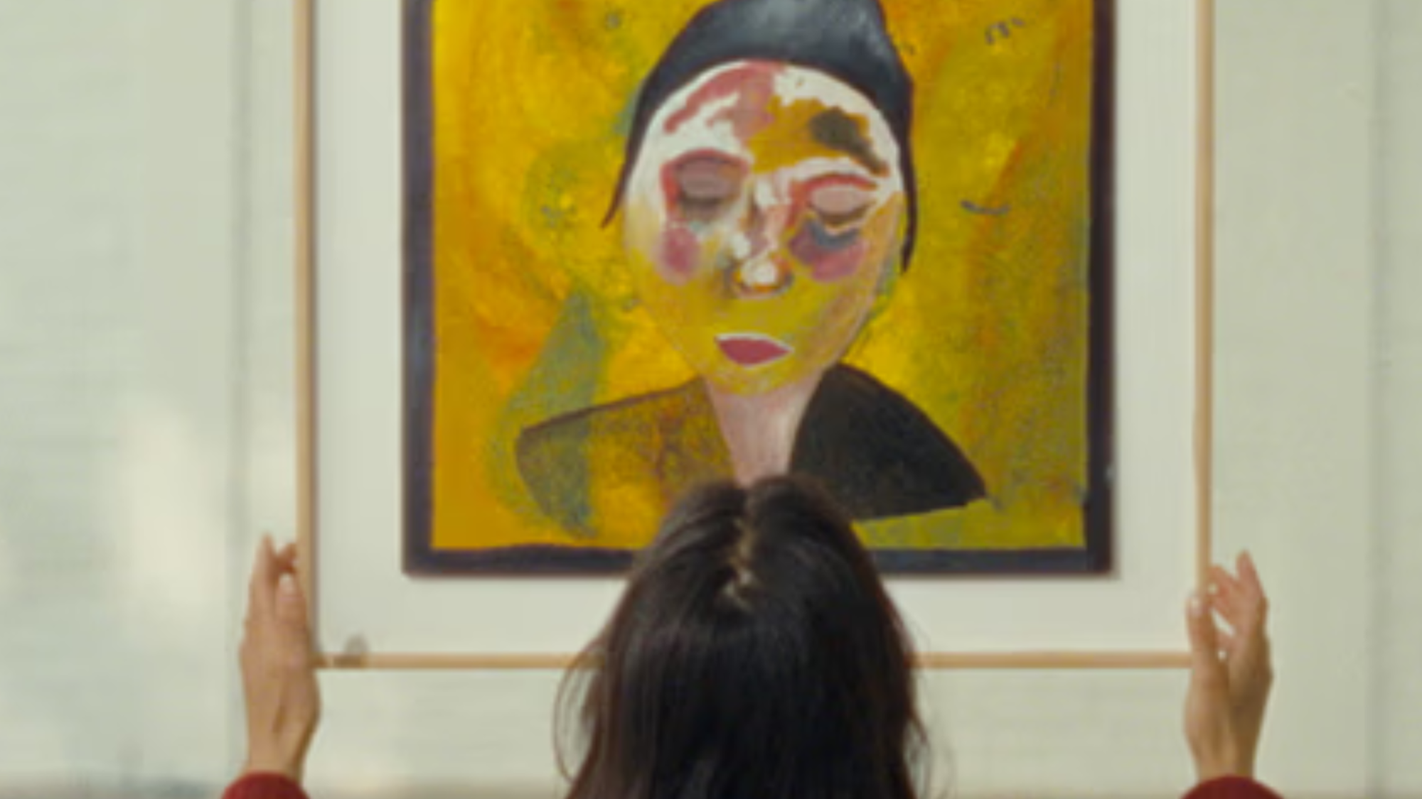 Vrouw kijkt naar een geel schilderij van een vrouw met een hoedje dat ze in haar handen heeft