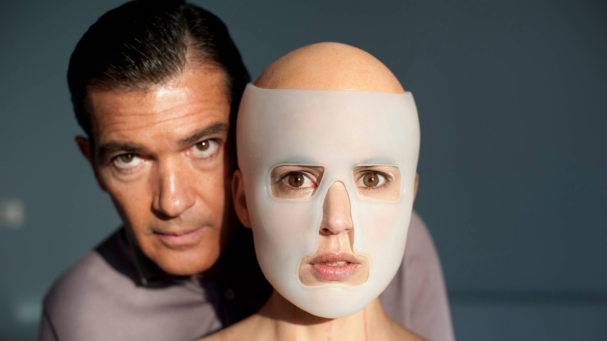 De hoofdpersonages uit La piel que habito kijken naar de camera, de vrouw heeft een doorzichtig masker op