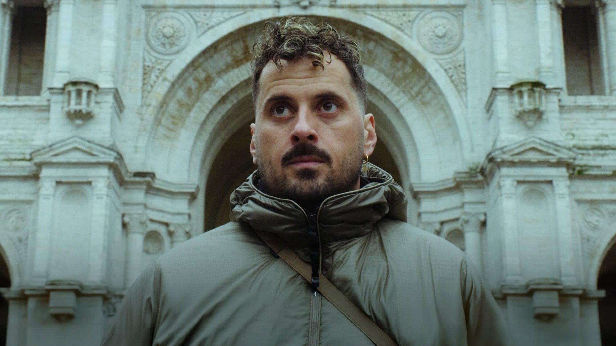 Zwangere Guy staat voor een gebouw en kijkt net langs de camera