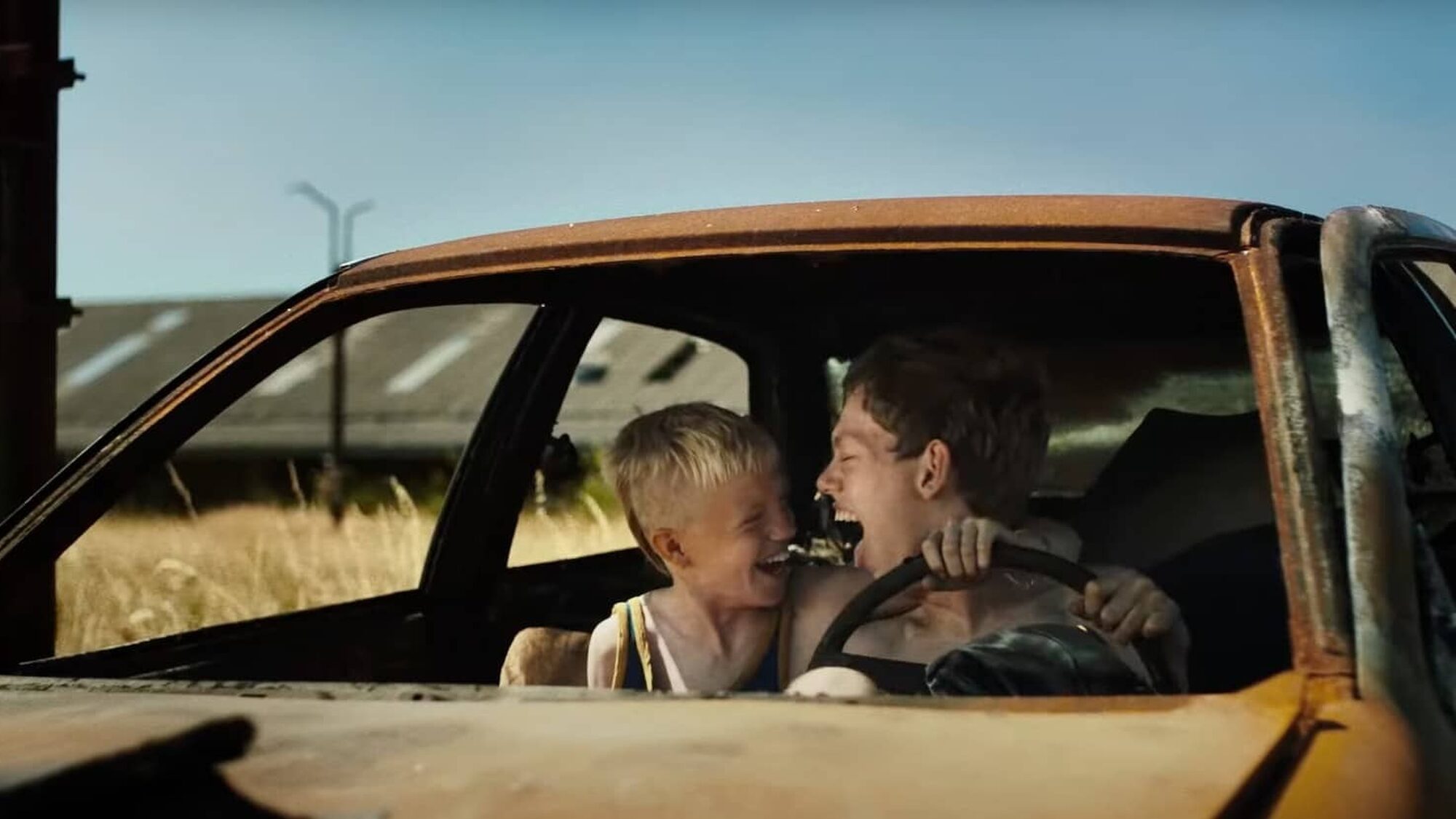 Twee broers zitten in een vervallen auto en gieren het uit van plezier