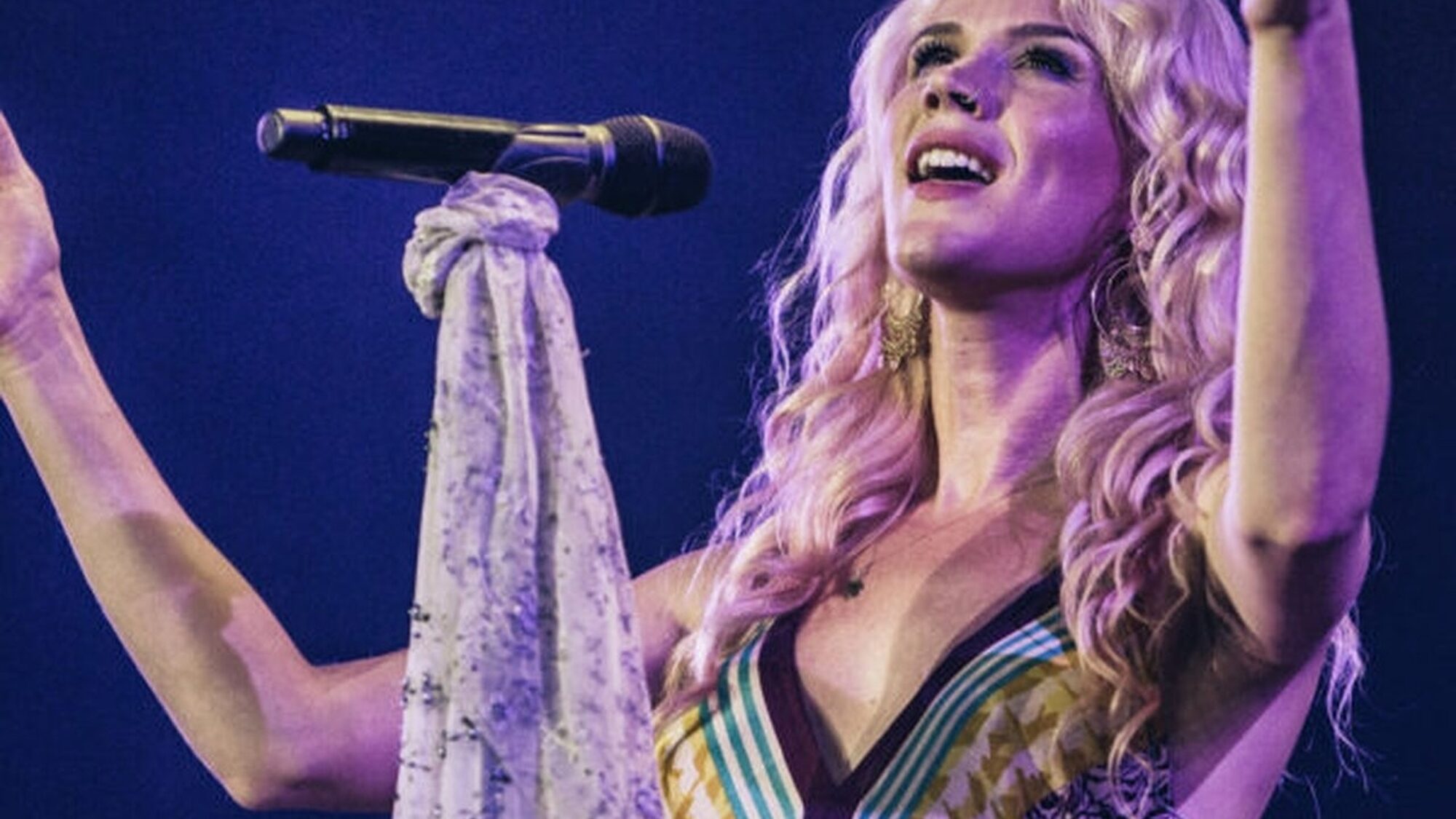 Zangeres Joss Stone zingt. Ze kijkt naar boven en spreidt beiden armen omhoog.
