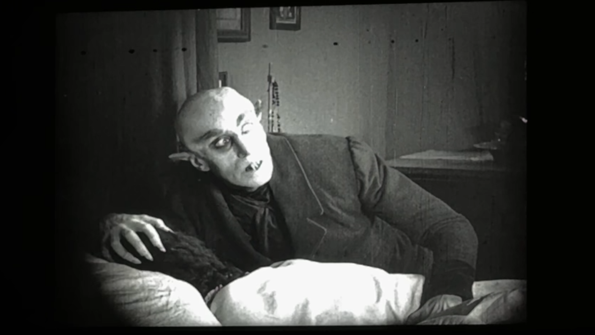 Een stilbeeld uit de film Nosferatu. We zien een griezelig figuur, een vampier, opveren uit een bed.