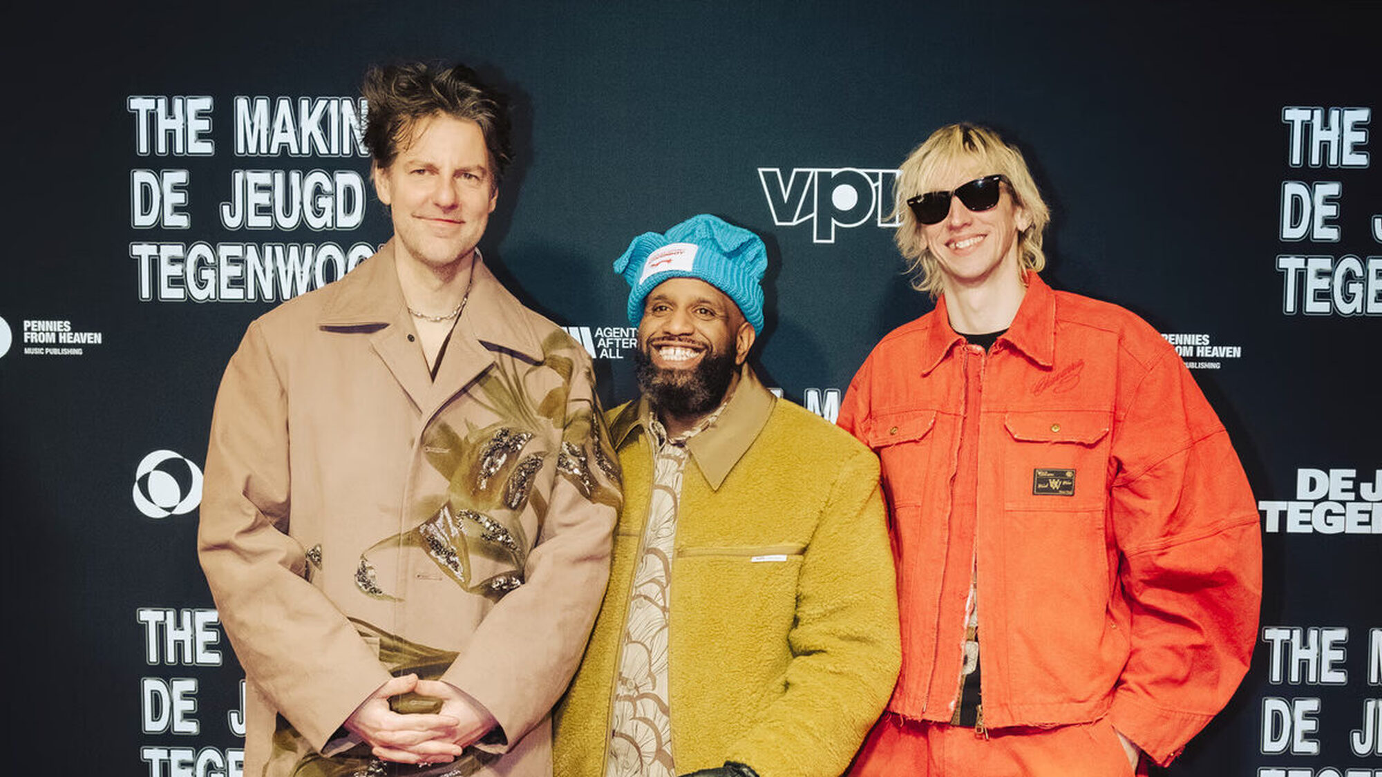 De drie mannen van de jeugd van tegenwoordig staan lachend naast elkaar voor een doek van hun eigen film