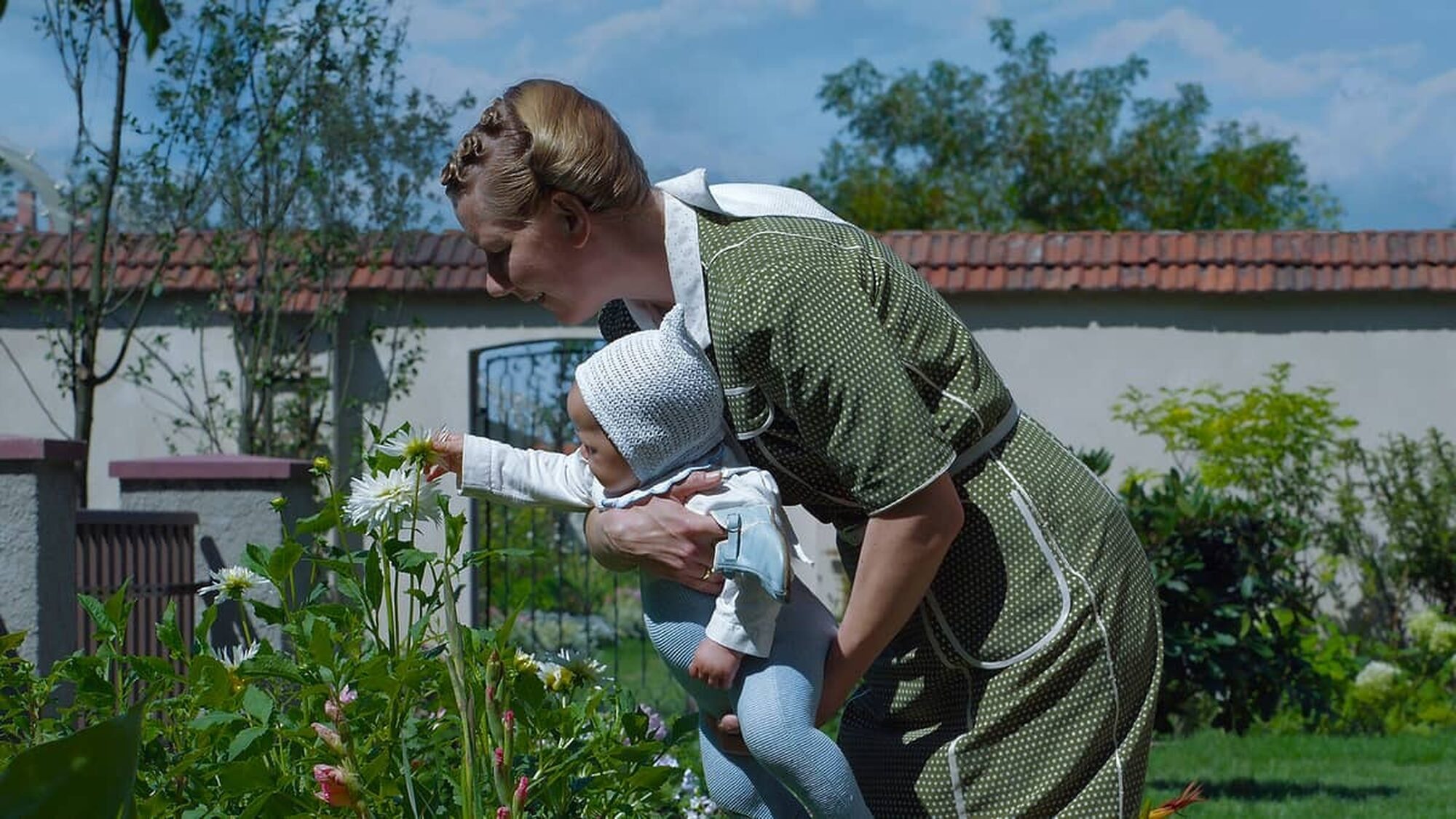 Vrouw in een groene jurk staat met haar baby in haar armen in een mooie groene tuin