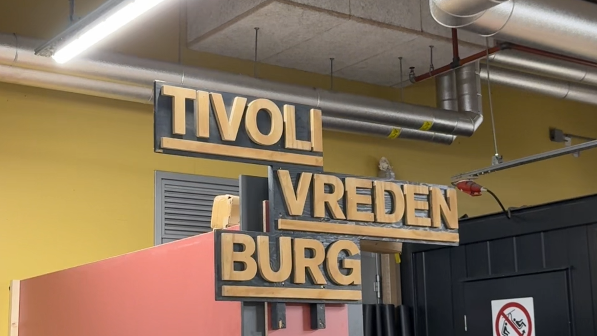 Een bord van uitgezaagd letters waar TivoliVredenburg staat. Het staat tussen allemaal andere spullen, alsof het in een opslag staat.