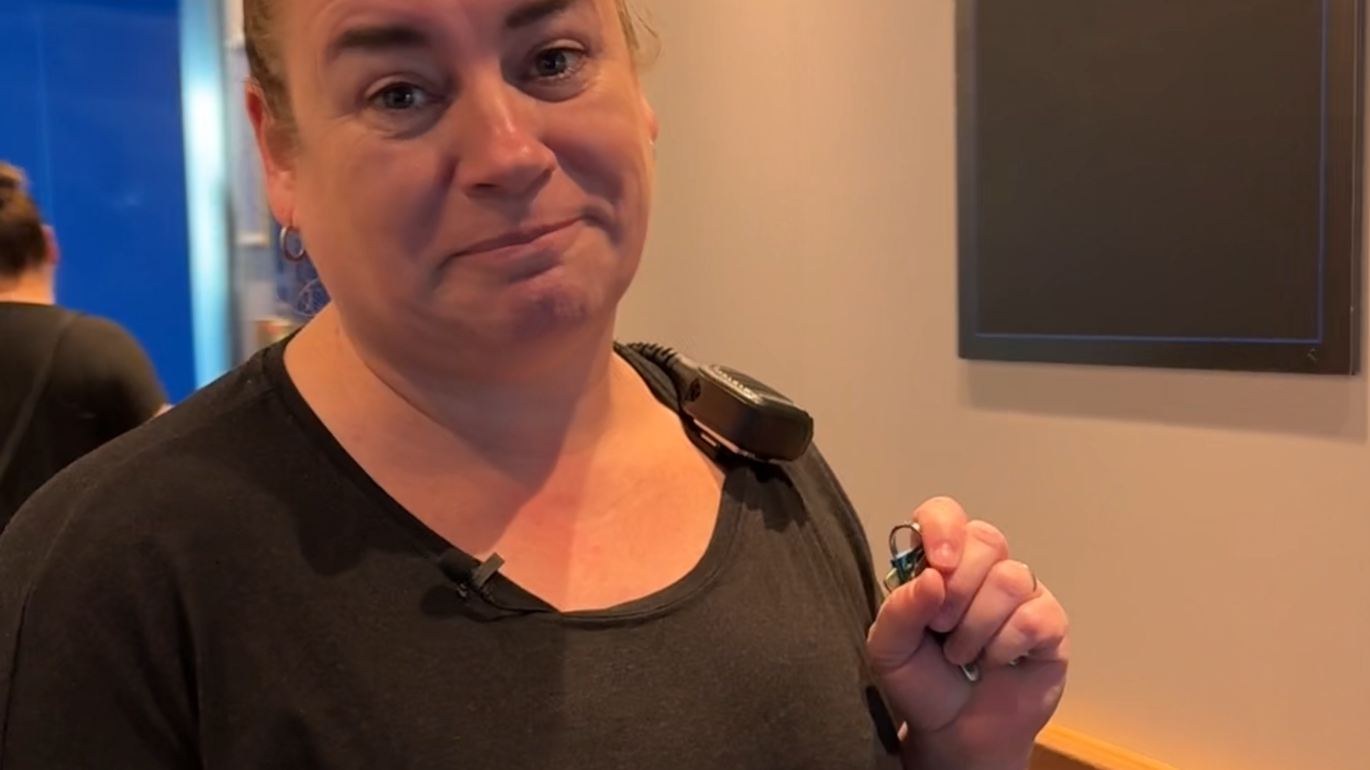 Een foto van Ilja, die de vragen in de tekst beantwoordt. Ze kijkt vriendelijk de camera in. Ze staat ergens in een gang en heeft zwarte kleren aan en een walkietalkie op haar schouder.