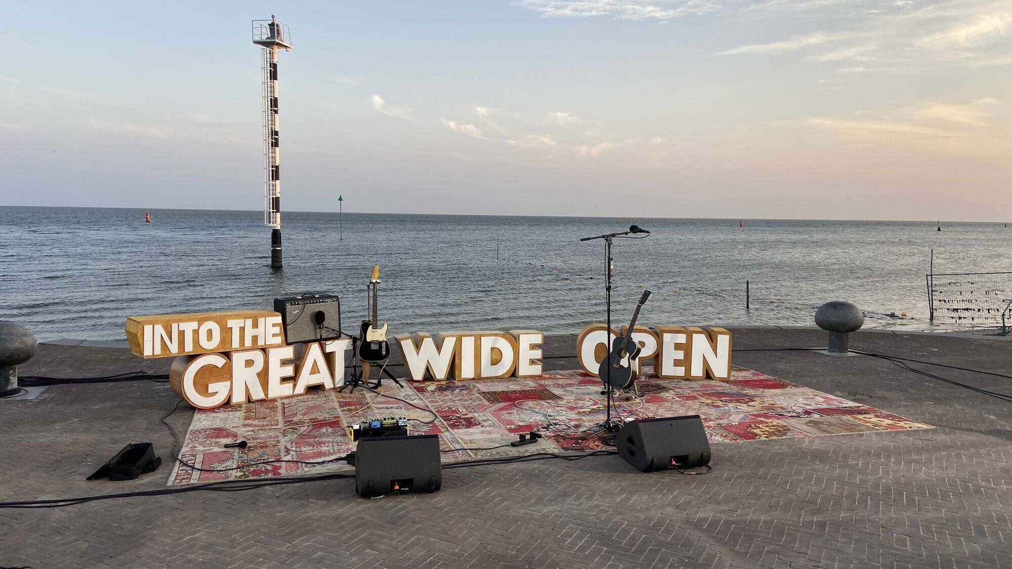 een foto van een band opstelling met op de achtergrond de zee. er staan grote letters 'into the great wide open'