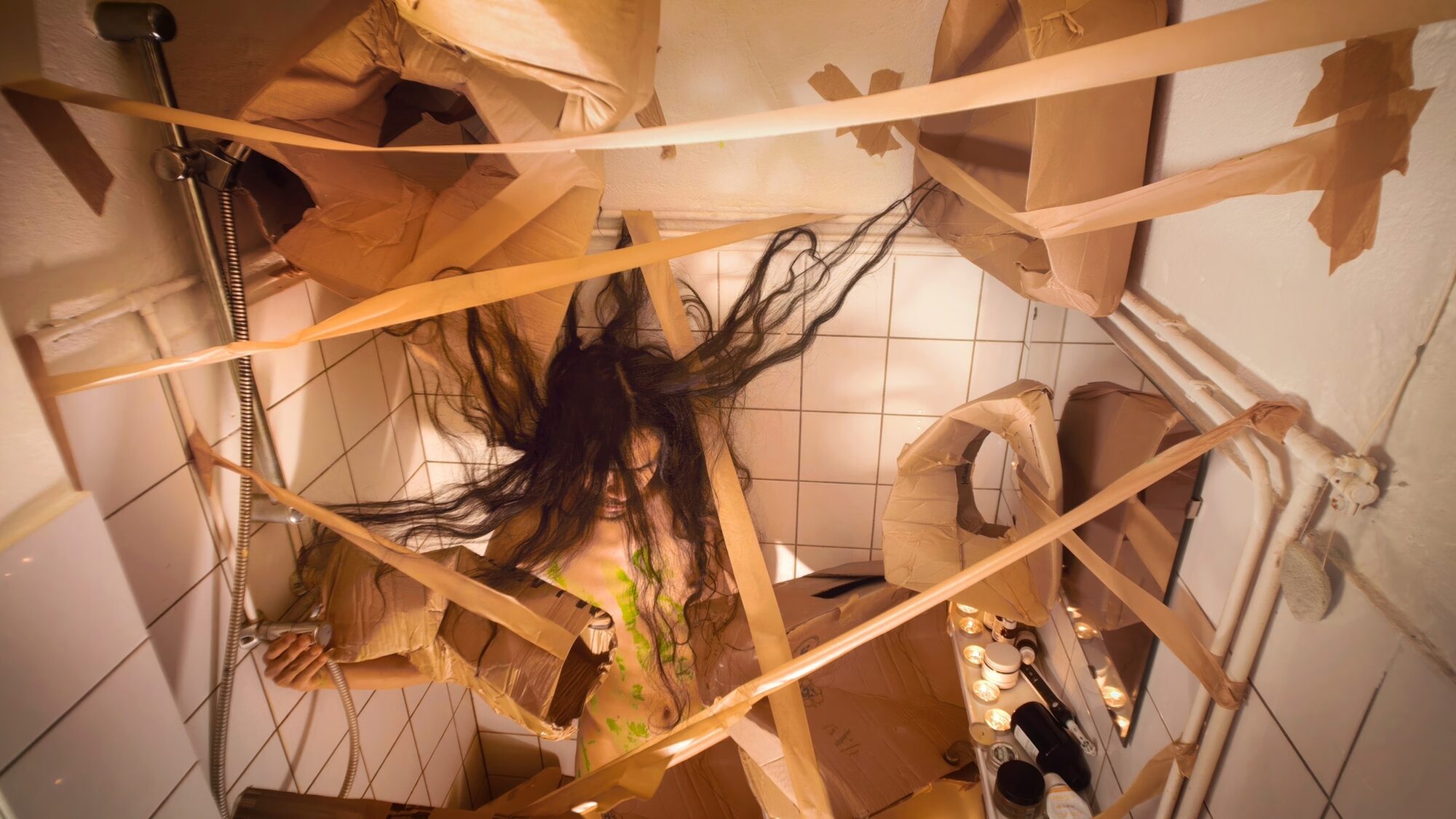 kunstenaar Nadh staat in de douche, waar hij allerlei kartonnen dozen en tape aan de muur heeft bevestigt.