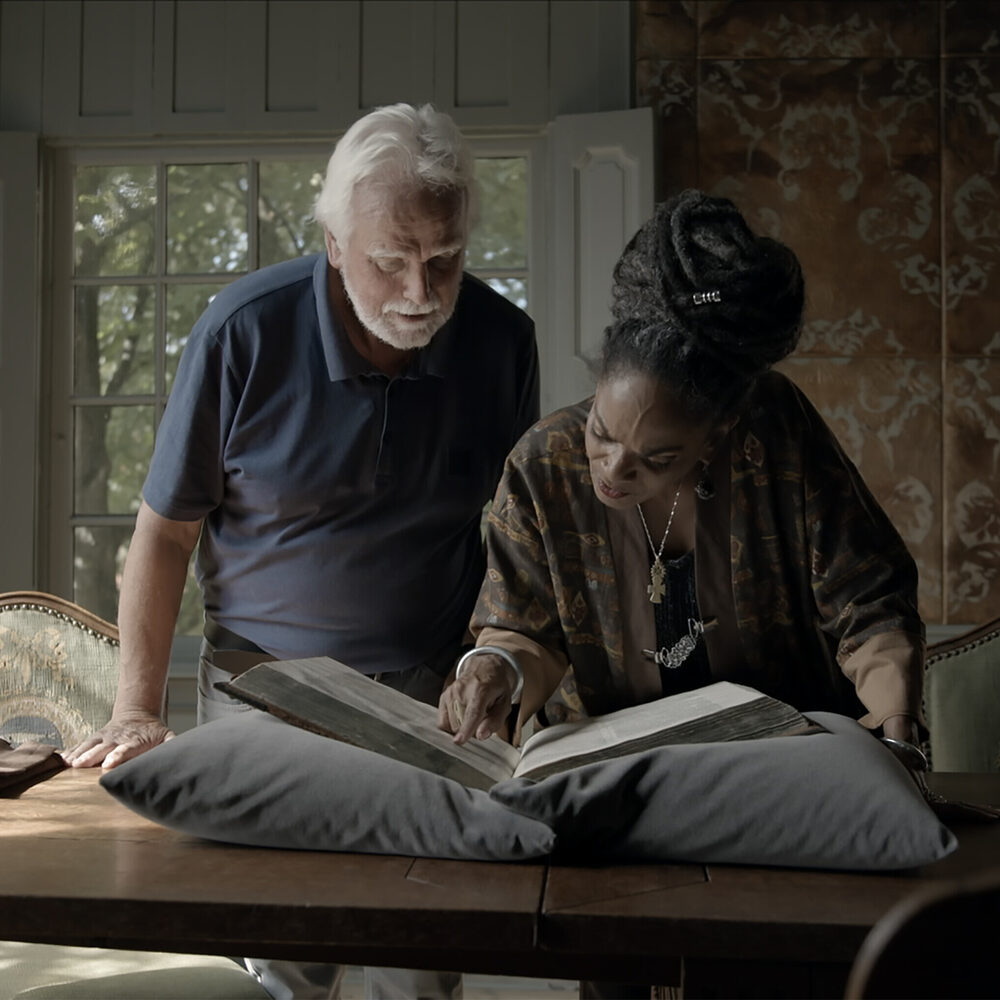 Presentatrice Aldith Hunkar en een man kijken samen met een oudere man in een historisch boek.