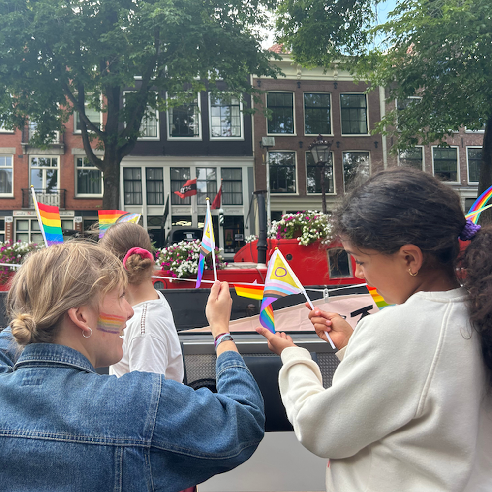 Een meisje en een mevrouw van Theater De Krakeling zwaaien met vlaggetjes naar de voorbijgangers vanaf de boot in Amsterdam.