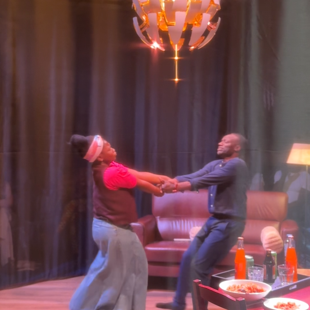 Op deze foto zien we de vader en dochter uit het toneelstuk dansend op het toneel. Er is een kleine woonkamer nagemaakt, met een tafel en stoelen en een bank met lamp ernaast.