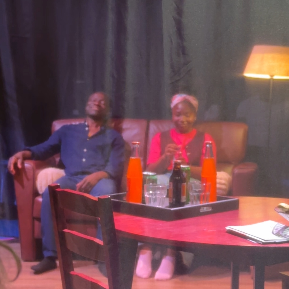 Op deze foto zien we de vader en dochter uit het theaterstuk op de bank op het toneel zitten. Er hangt een gaasdoek tussen ons en het podium in.