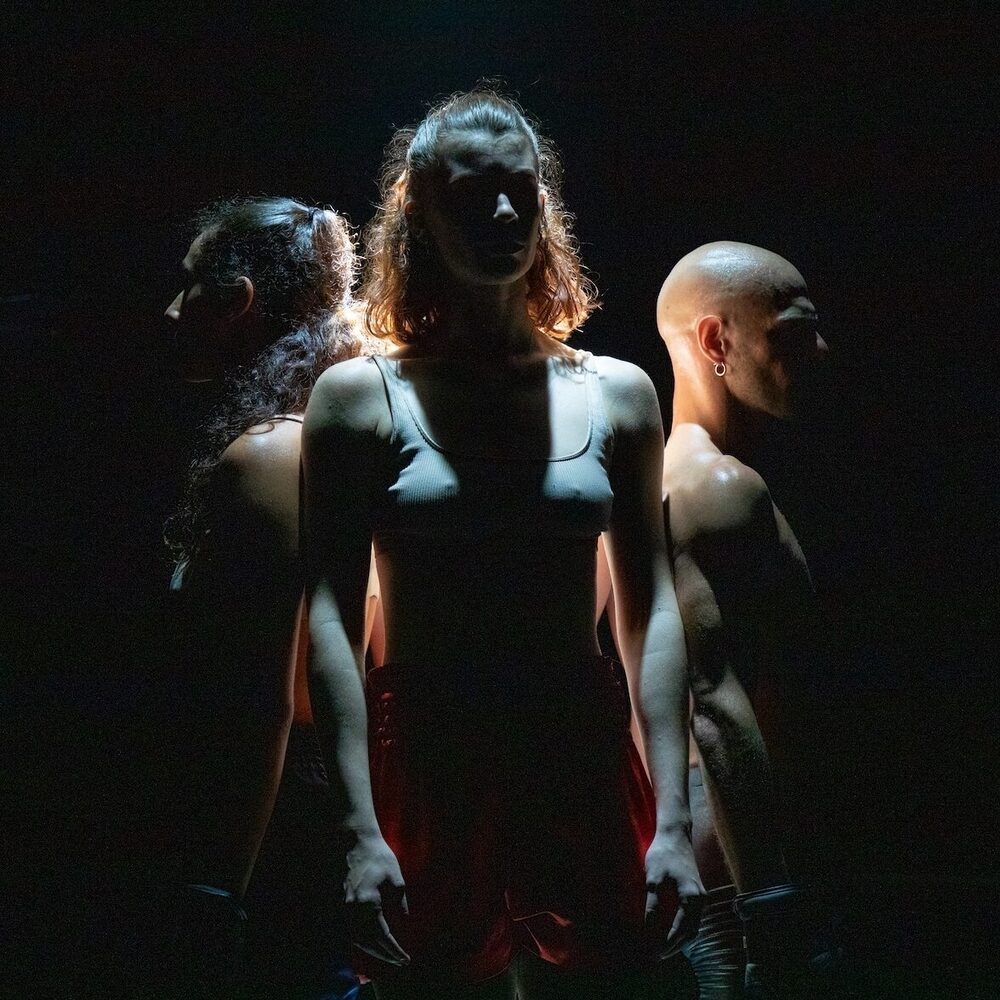 Drie dansers staan op een donker toneel.