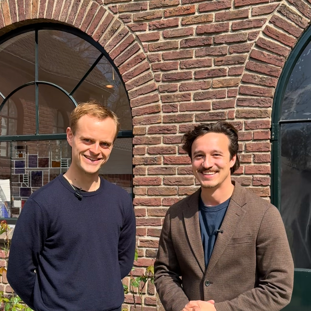 Foto van de twee hoofdrolspelers, Coen en Jurriaan. Ze staan voor een stenenmuur en kijken allebei vriendelijk de camera in.