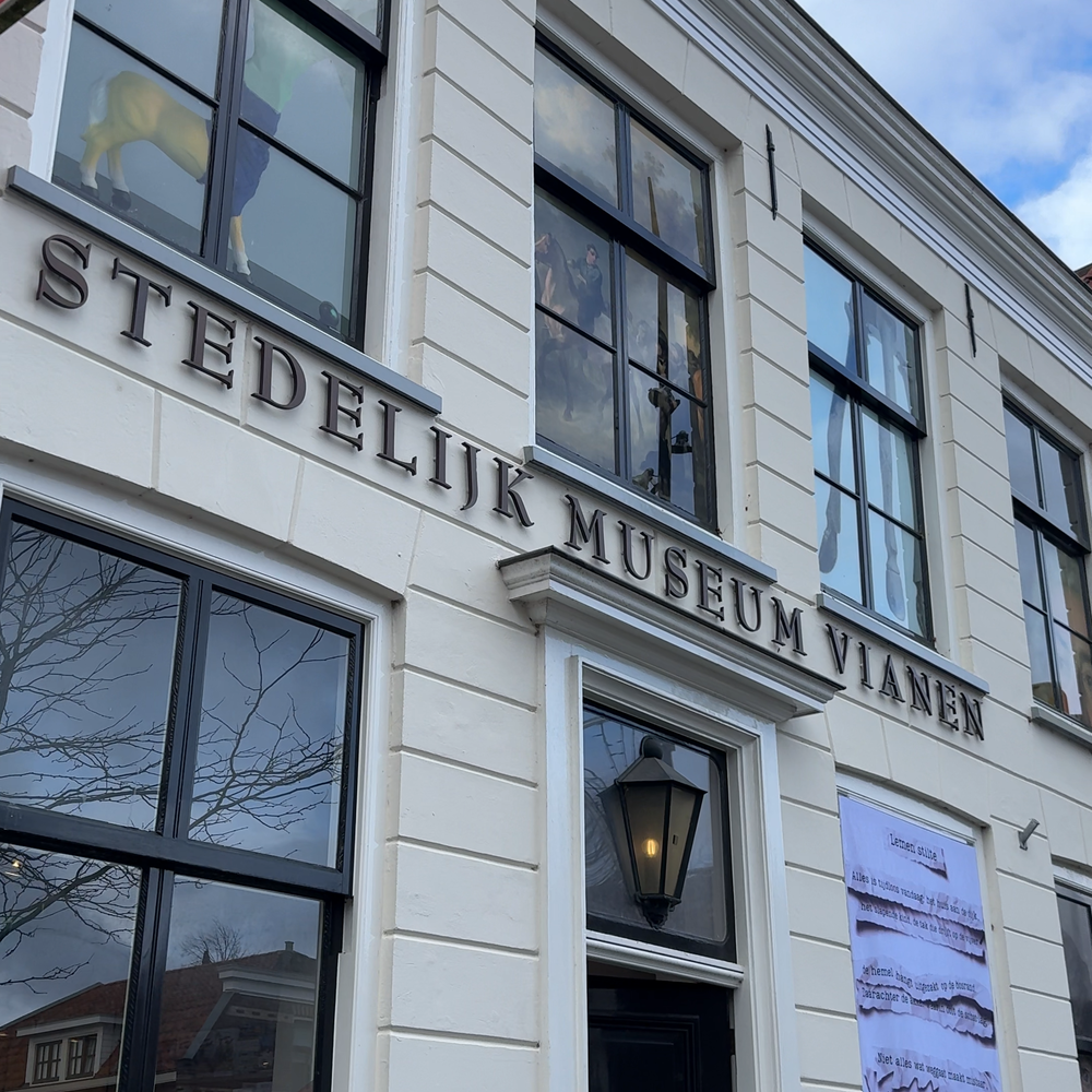 Een foto van de gevel van het stedelijk museum vianen. Het is een wit gebouw met grote letters boven de deur STEDELIJK MUSEUM VIANEN.