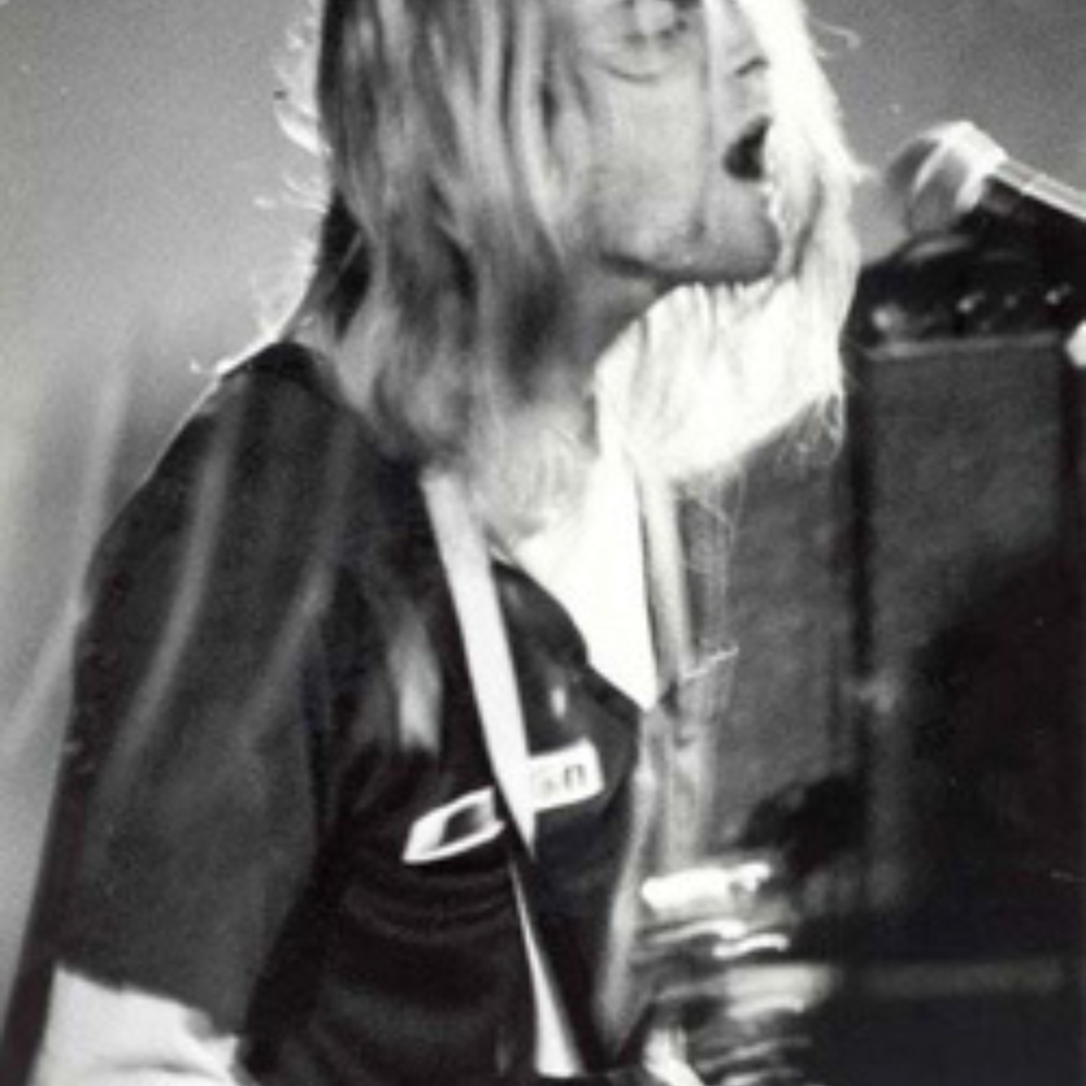Foto van Kurt Cobain van Nirvana in VERA. Het is een zwart wit foto van een man met lang blond haar en een gitaar in zijn handen. De foto is van erg dichtbij gemaakt.