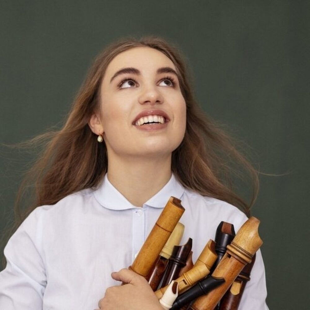 Muzikant Lucie Horsch kijkt omhoog met een aantal blokfluiten onder haar arm geklemd.