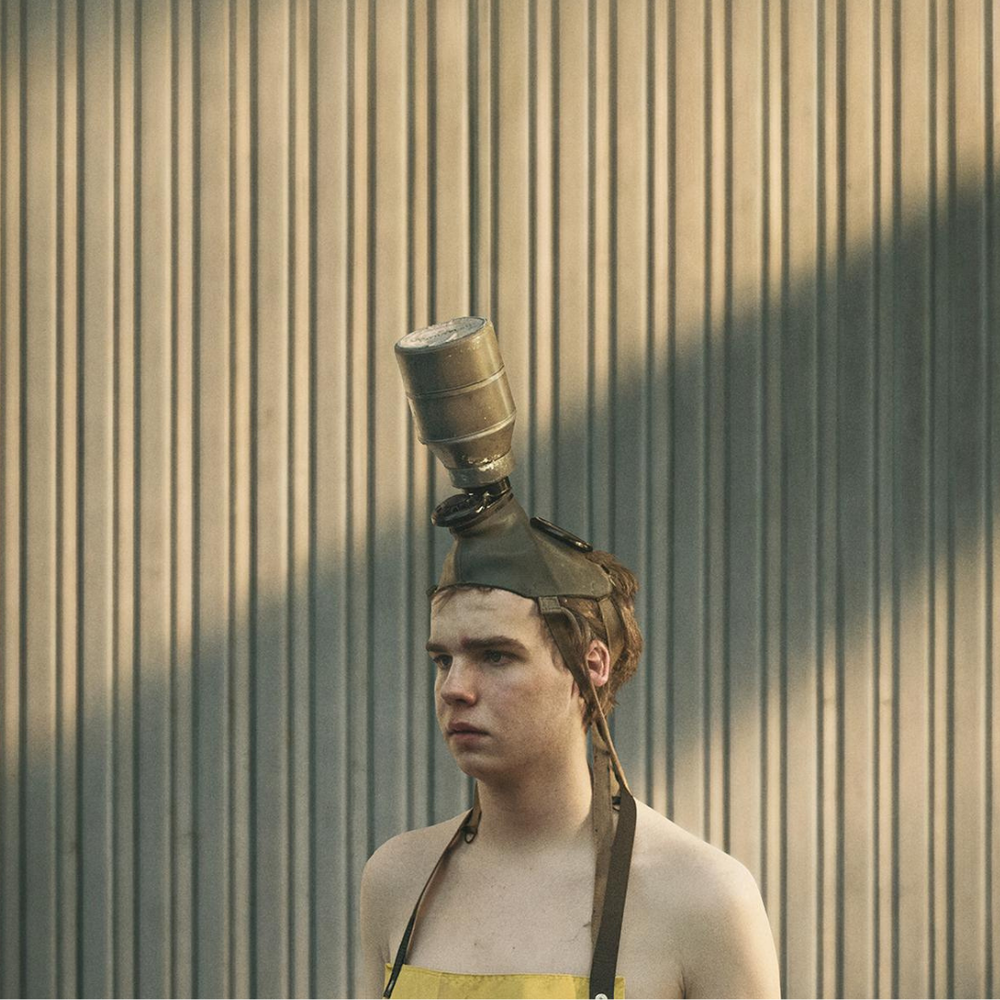 Jongen met schort om en een gasmasker op kijkt naar iets buiten beeld