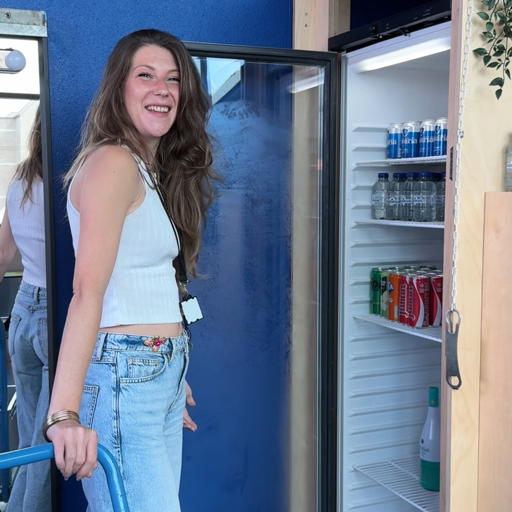 Een foto van Nikki bij een koelkast. Ze kijkt lachend de camera in.