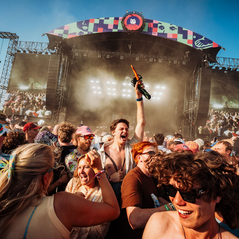 Een foto van een hossende mensenmassa voor het grote Pinkpop podium, in de zon.