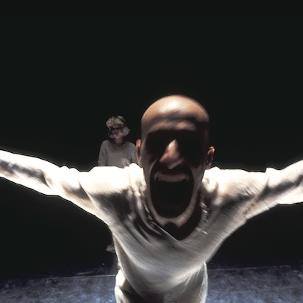 Danser schreeuwt en loopt met gespreide armen op de camera af.