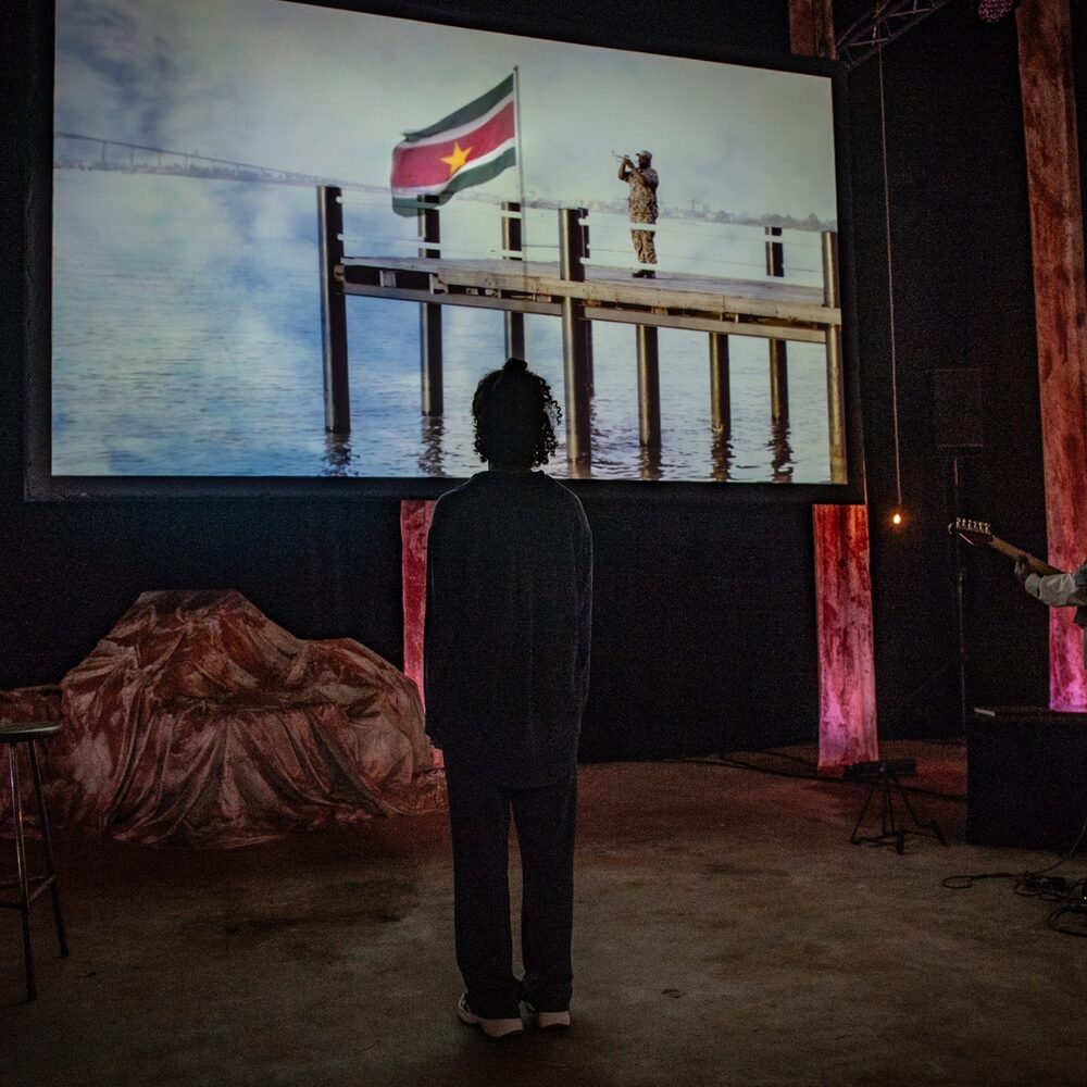 Een stil uit het theaterstuk Meer dan Bauxiet. twee mensen op hun rug gezien, staan voor een scherm