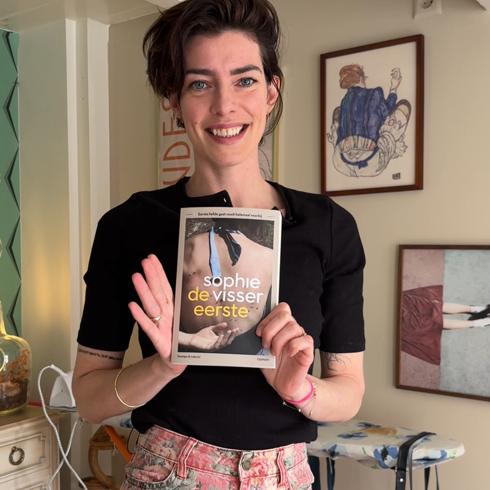 Schrijfster Sophie Visser staat met haar boek in haar handen. Ze laat het lachend aan de camera zien.