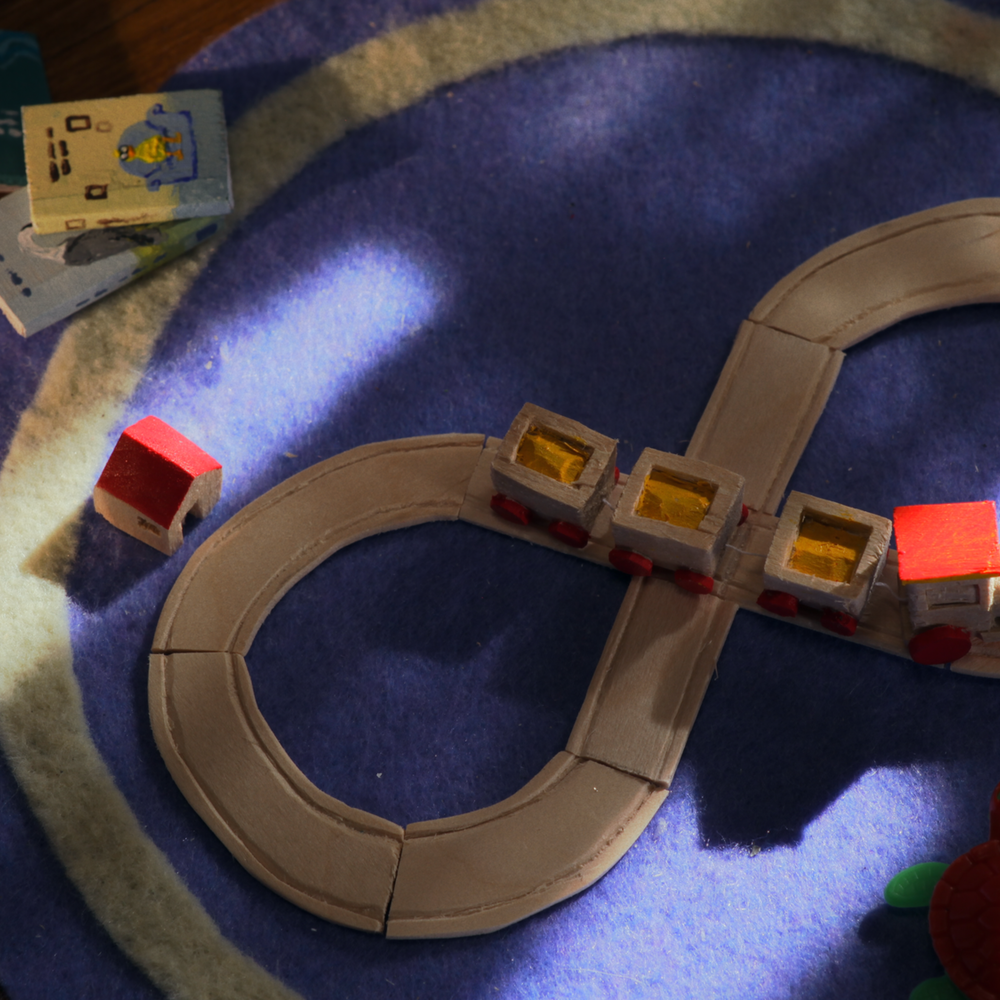 Een stil van een stop motion beeld uit spijtmoeders. het is een houten speelgoedtrein op een houten spoor op de grond op een kleed.