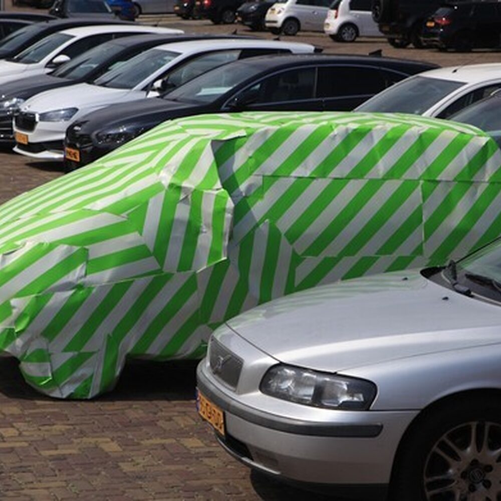 Een foto van een rij auto's. Een van de auto's is ingepakt in groen-wit gestreepd cadeaupapier.