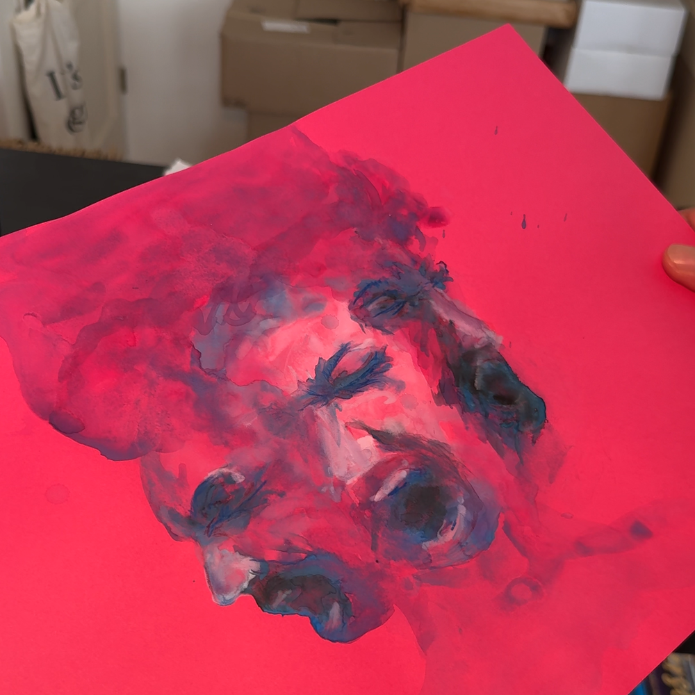 Dean laat het schilderij wat zijn vriendin voor de cover heeft gemaakt zien. Het is een felroze stuk papier met 3 blauwe vage gezichten erop geschilderd.