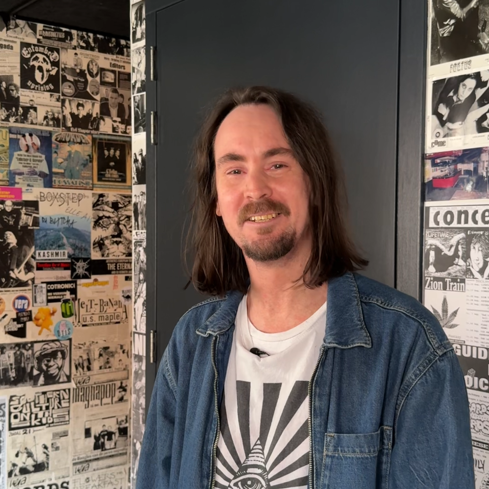 Portretfoto van artiestenbegeleider Mark. Mark kijkt vriendelijk de camera in en staat in een hal.