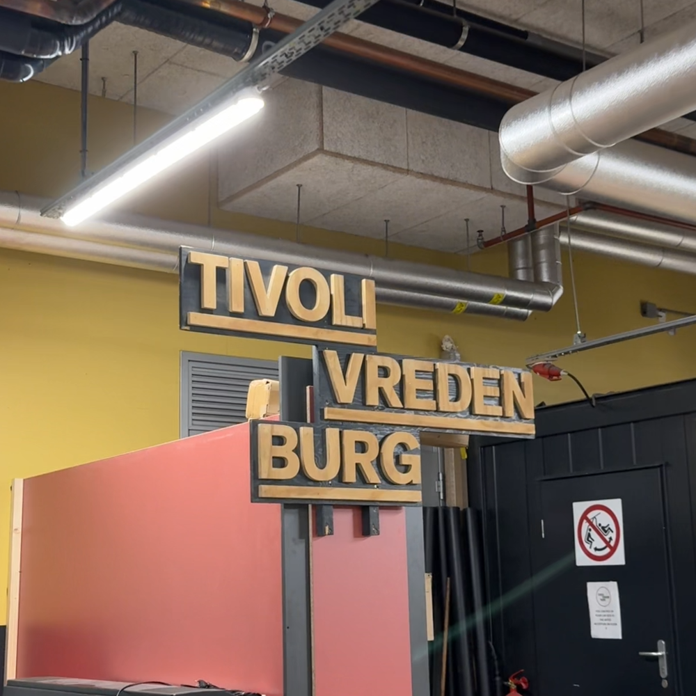 Een bord van uitgezaagd letters waar TivoliVredenburg staat. Het staat tussen allemaal andere spullen, alsof het in een opslag staat.