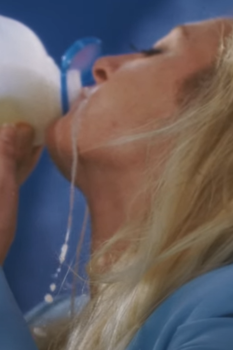 S10 drinkt hier van een pak melk en er druipt melk langs haar nek. Ze heeft een blauwe jas aan.