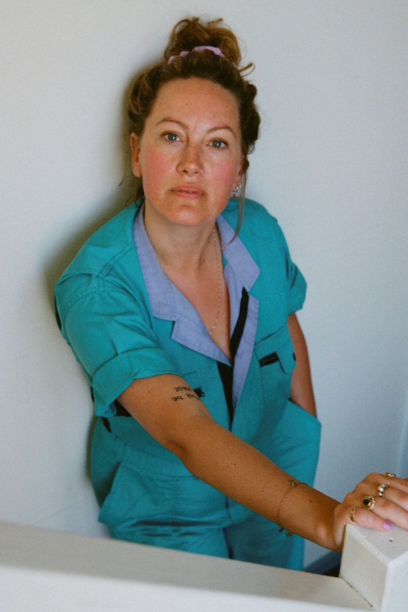 Actrice Laurien van Rijswijk staat tegen een witte muur. Ze draagt een blauwe overal en haar haar in een knot.