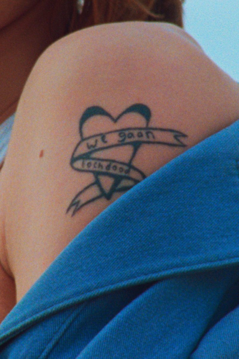 Blote schouder met tattoo. De tattoo is een hart met een lint eromheen, waarop staat 'We gaan toch dood'.