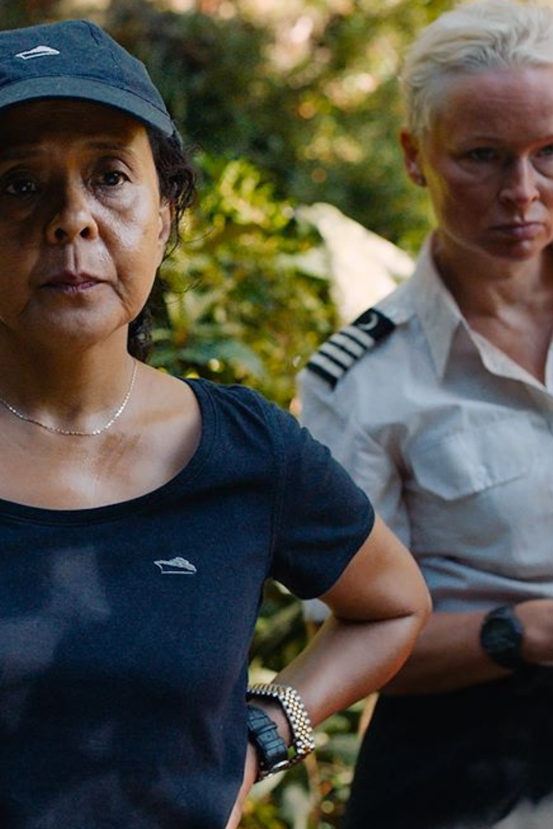 Er staan twee vrouwen op het beeld. De linker vrouw staat met haar handen in haar zij en heeft een zwart T-shirt aan en een zwarte pet op. De rechtervrouw heeft kort geblondeerd haar en heeft een kapiteinkostuum aan.