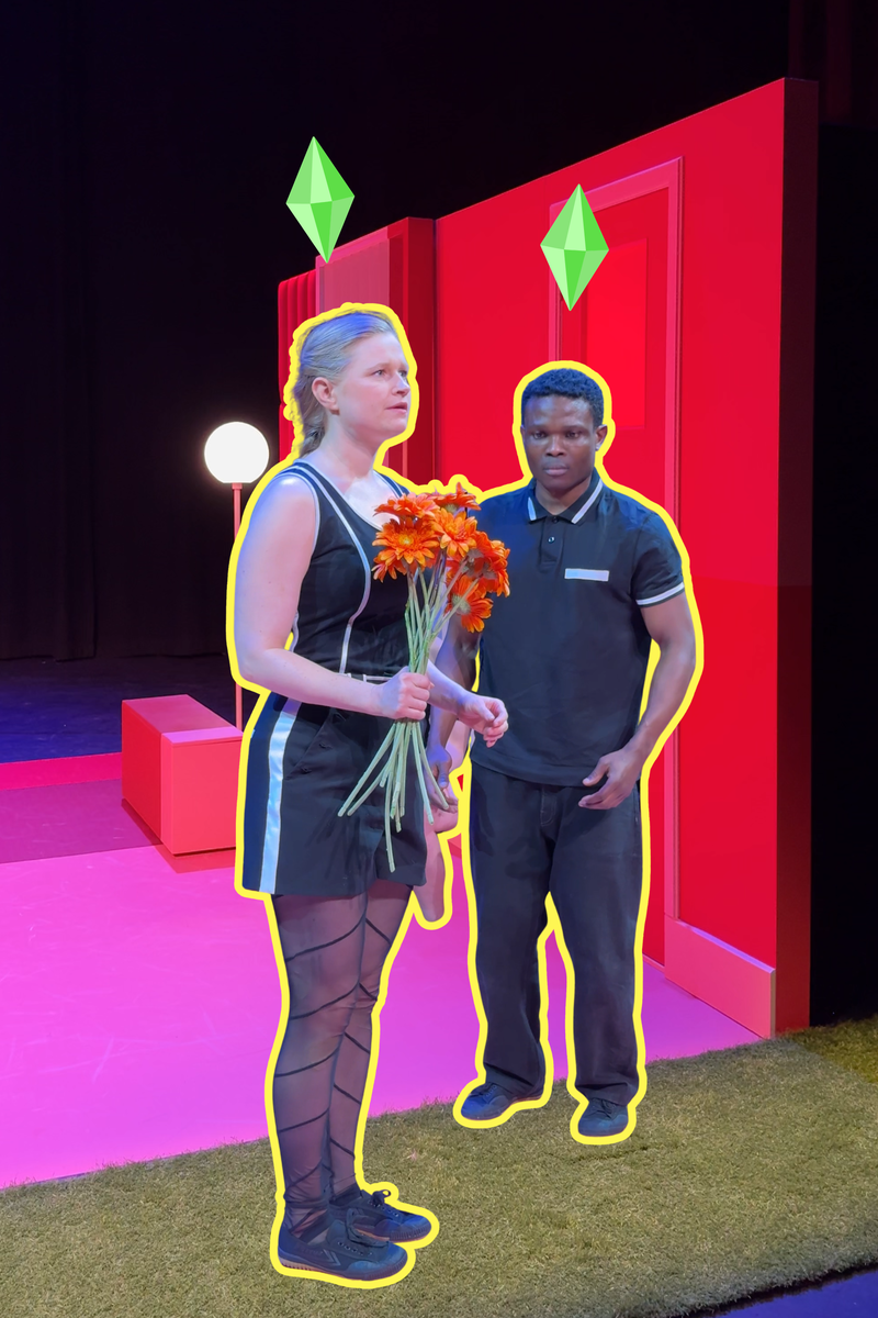 Een stil uit de voorstelling. we zien links een vrouw met oranje bloemen in haar hand en rechts een man die naar de bloemen kijkt. Ze staan stil alsof ze poppen zijn. Het decor waar ze instaan is roze en oranje.