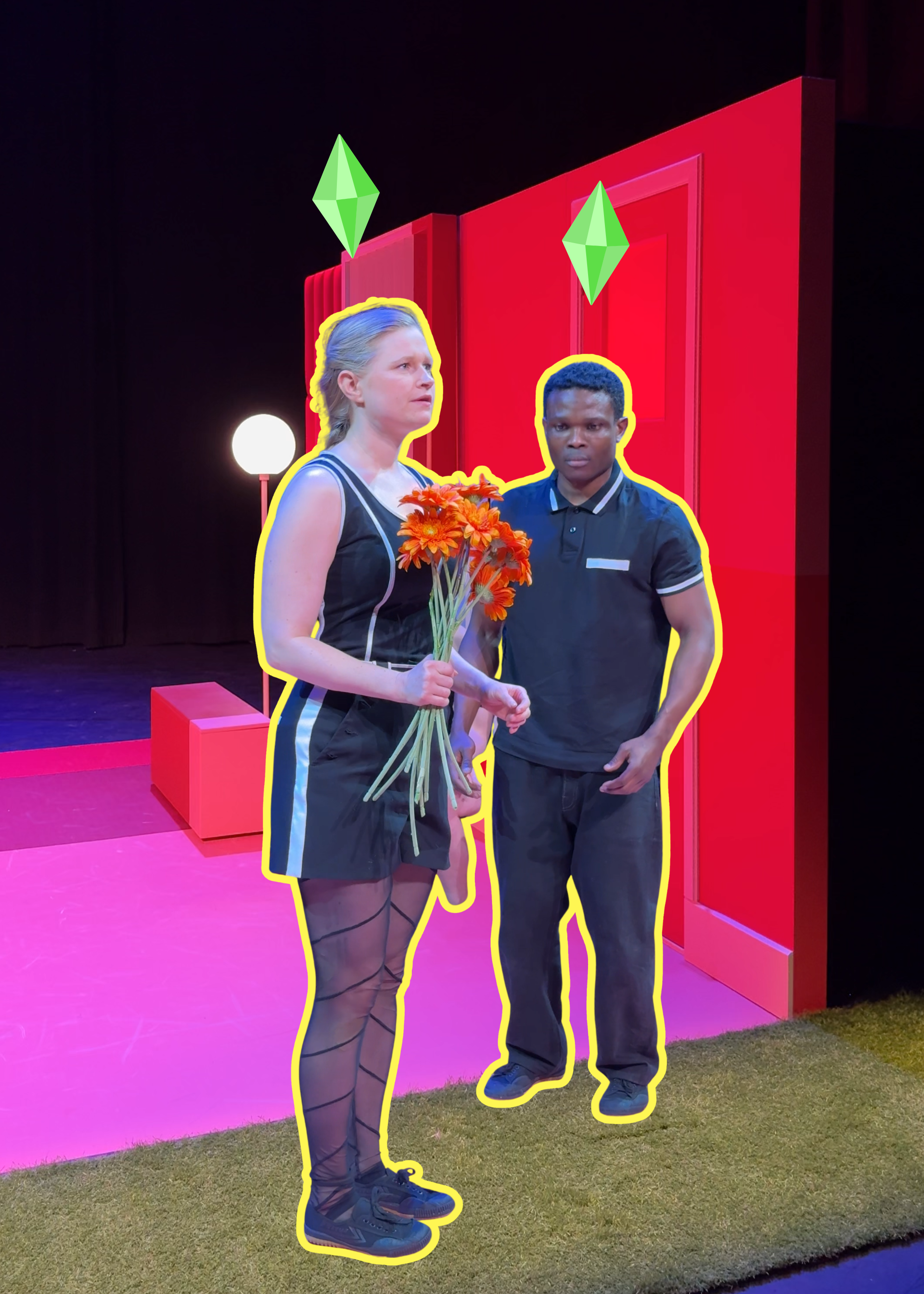 Een stil uit de voorstelling. we zien links een vrouw met oranje bloemen in haar hand en rechts een man die naar de bloemen kijkt. Ze staan stil alsof ze poppen zijn. Het decor waar ze instaan is roze en oranje.