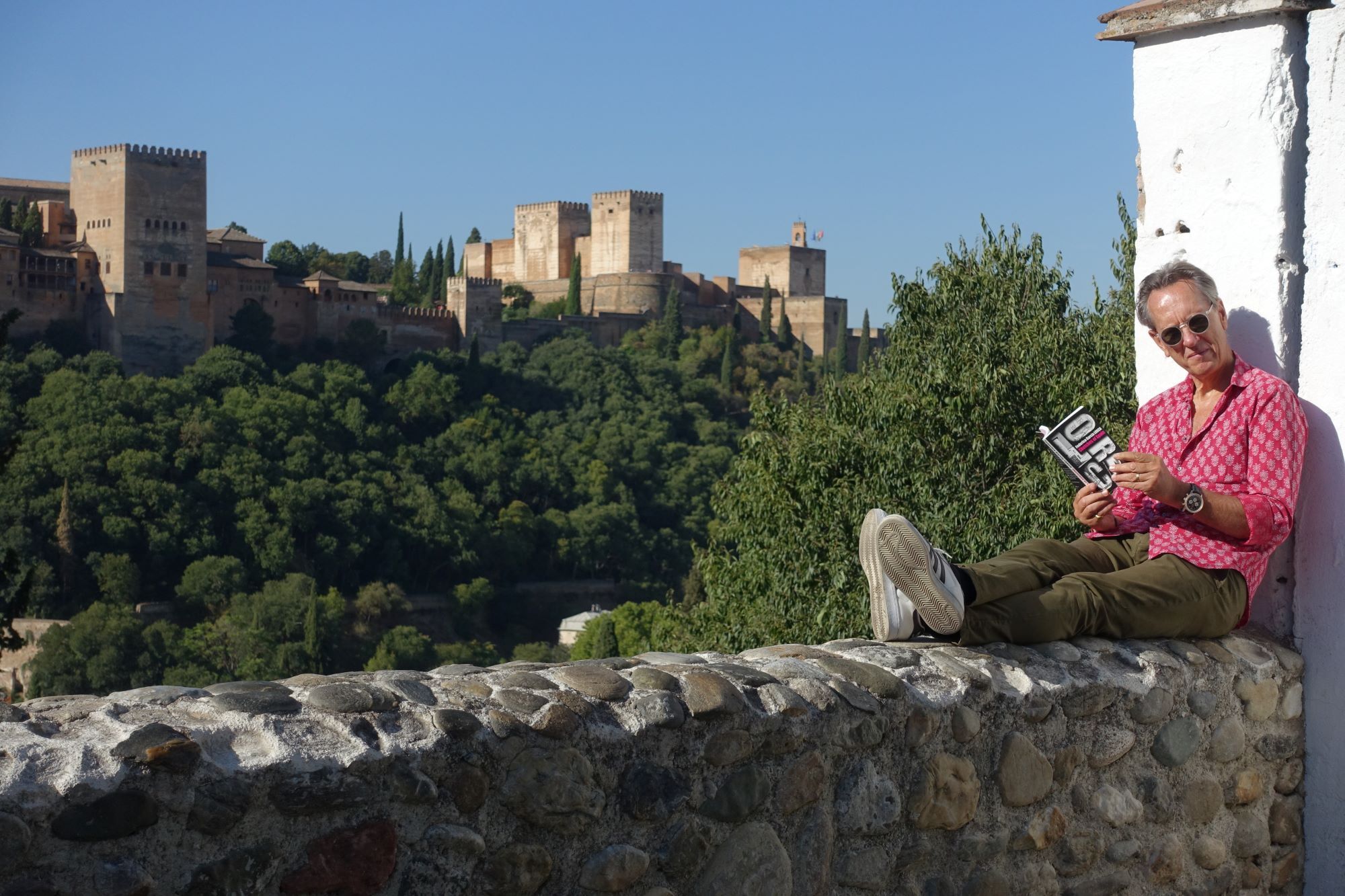 Richard E. Grant met boek in Spanje voor het Alhambra