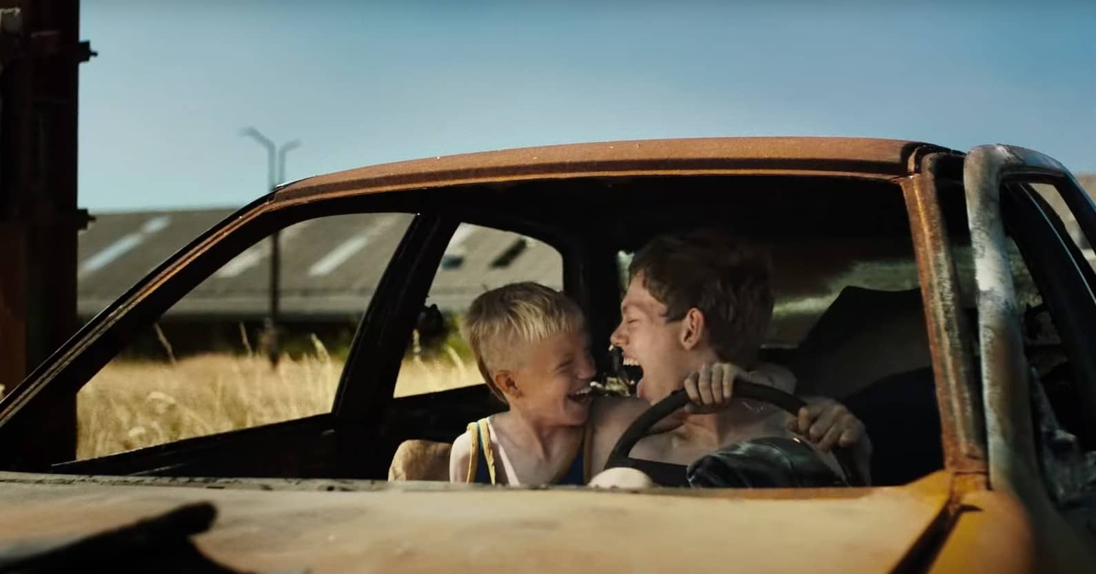 Twee broers zitten in een vervallen auto en gieren het uit van plezier