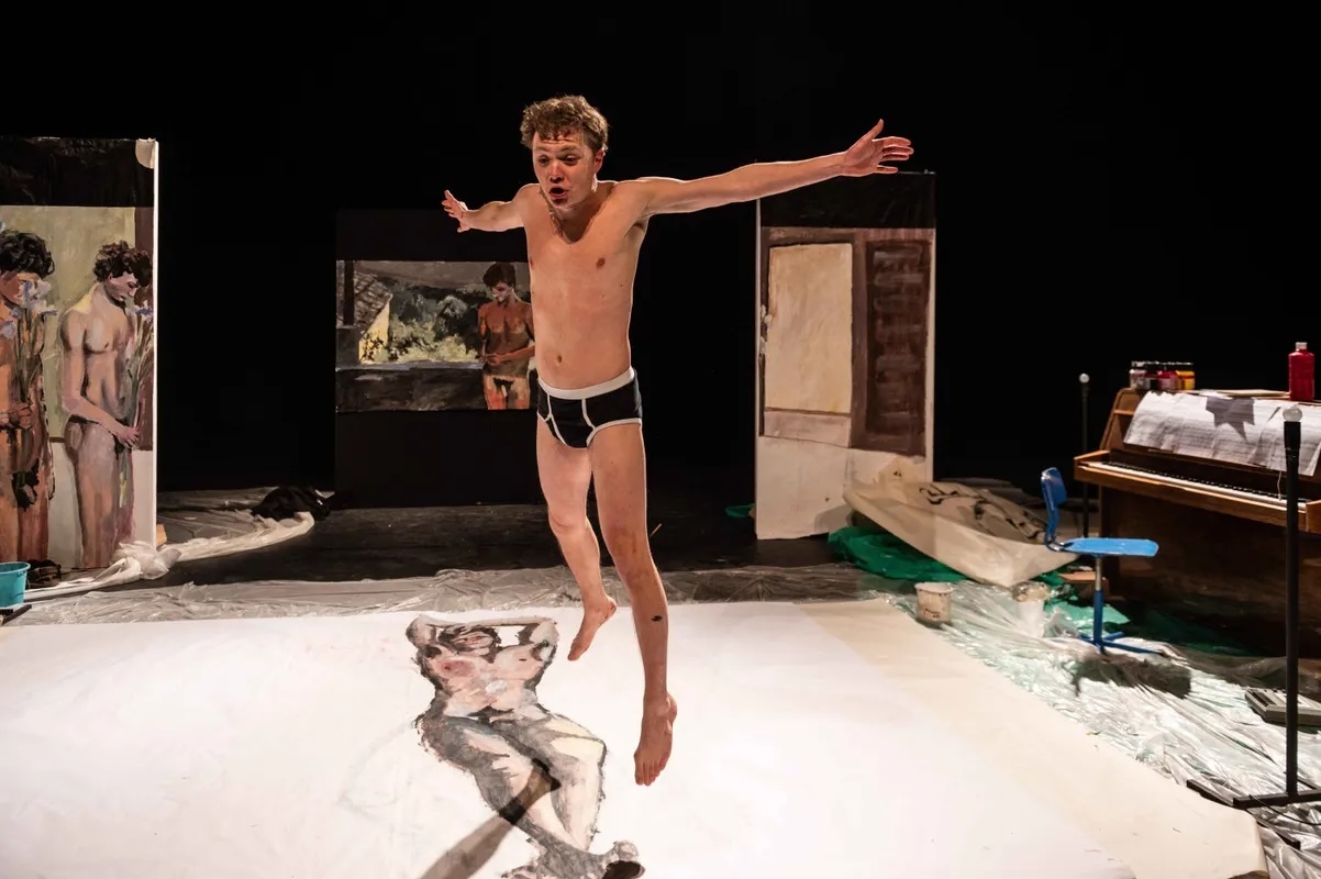 Witte jongeman springt in zijn onderbroek op het toneel op een schilderij met schilderijen op de achtergrond