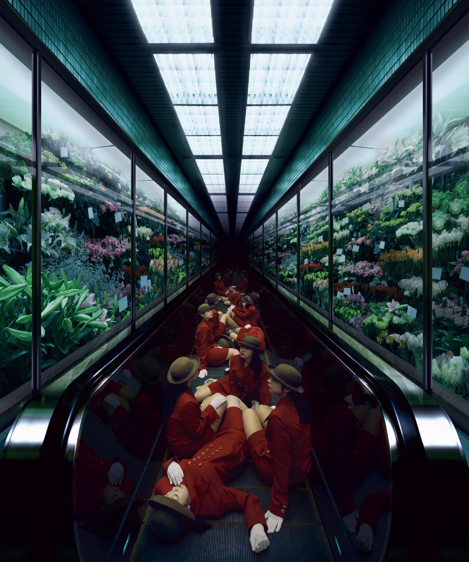 Een grote groep vrouwen met bruine hoeden, rode pakken en witte handschoenen zit en ligt op een roltrap. Om hen heen zijn aan beide kanten glazen wanden met allerlei verschillende bloemen.