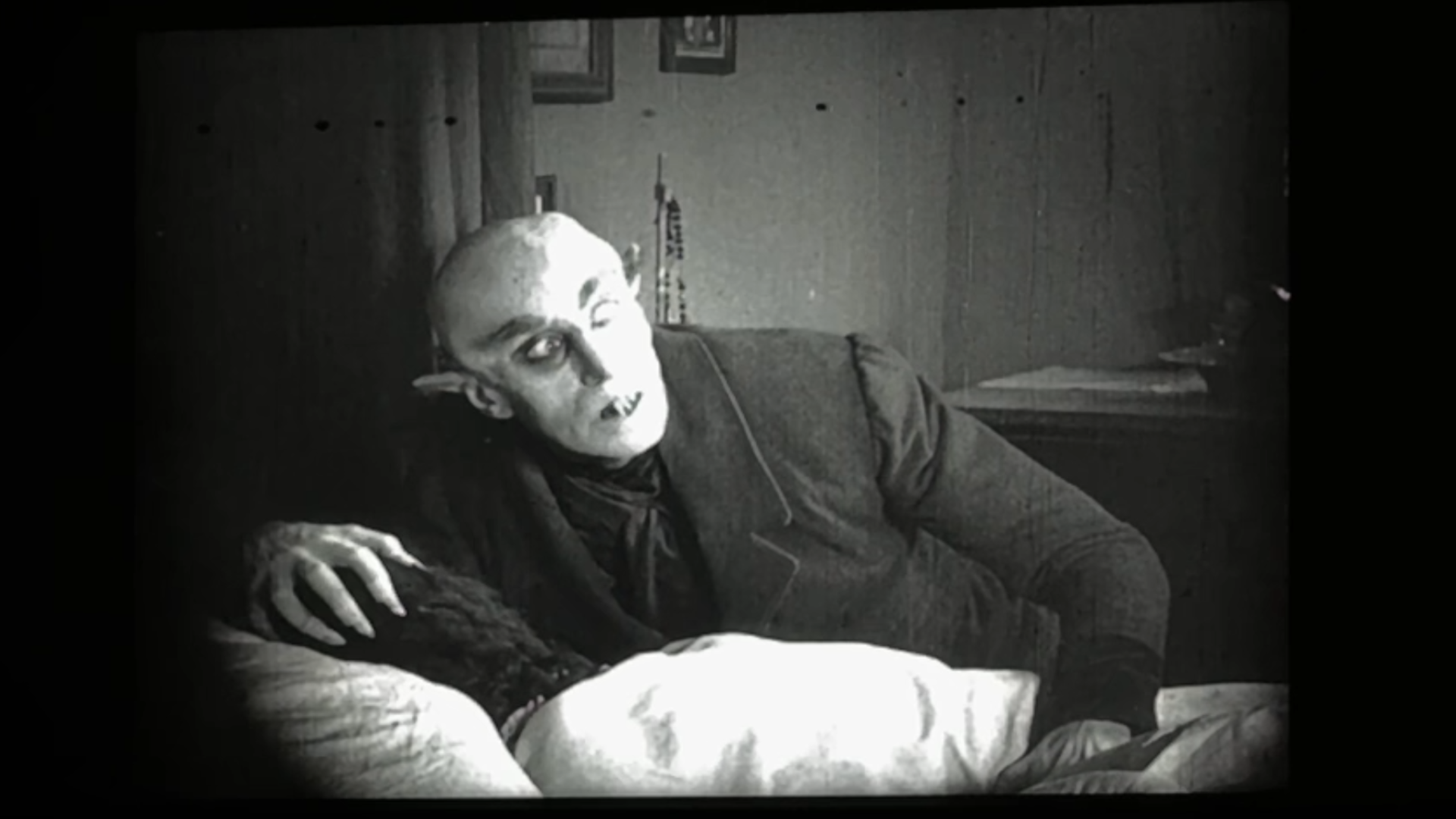 Een stilbeeld uit de film Nosferatu. We zien een griezelig figuur, een vampier, opveren uit een bed.