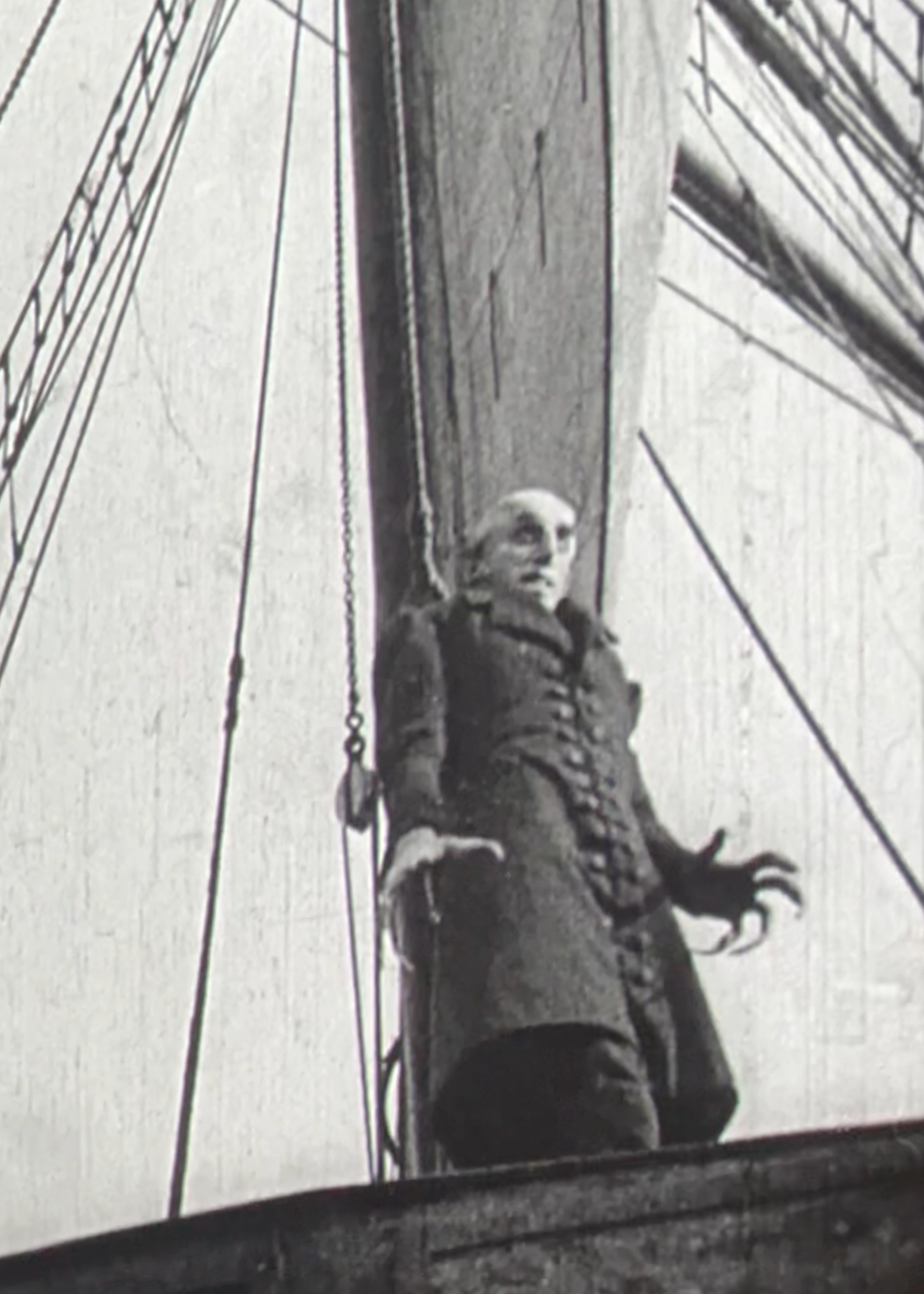 Een stil uit de film Nosferatu. We zien een griezelige man op een schip staan. Hij is erg lang en heeft hele lange vingers.