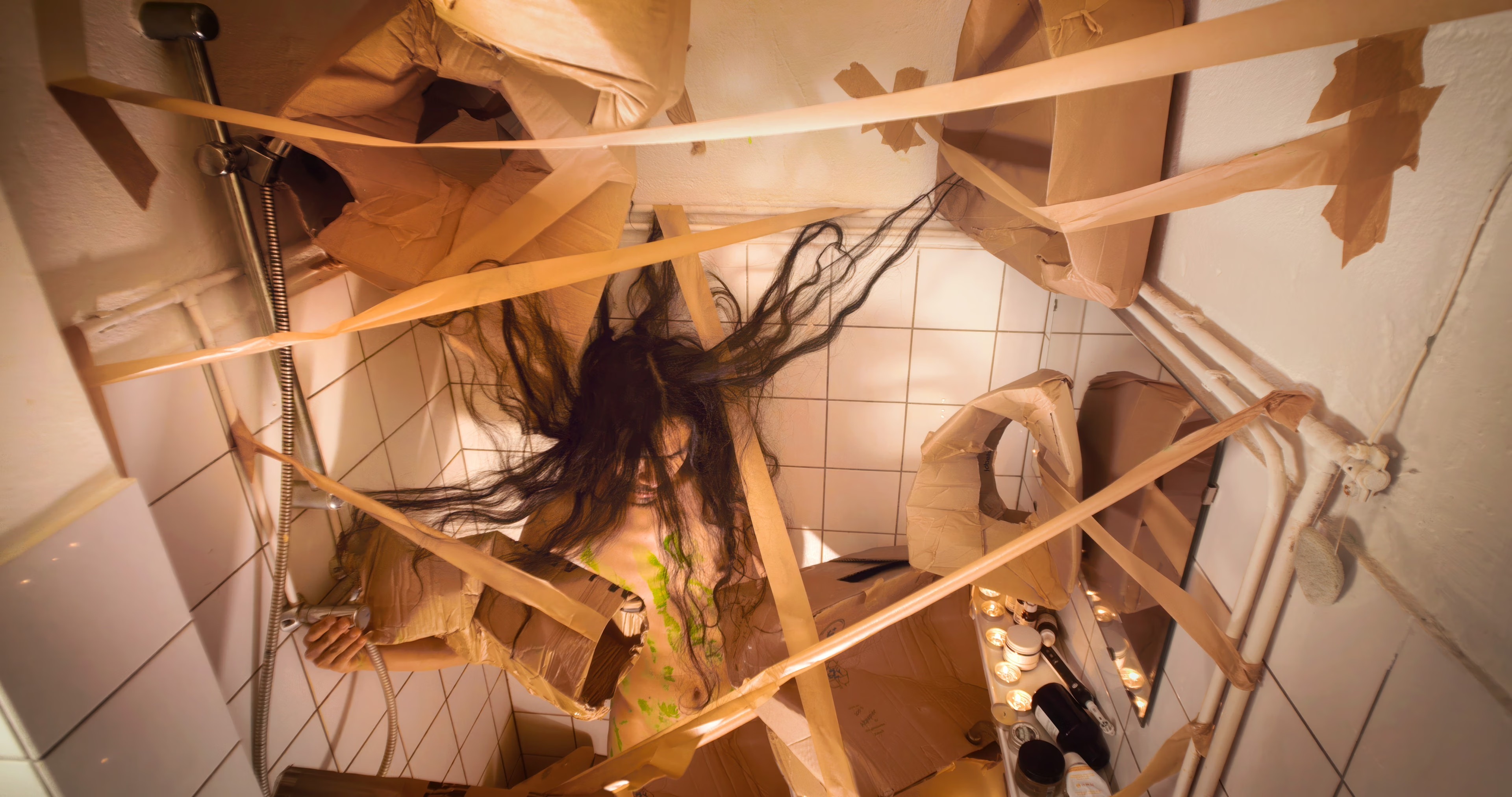 kunstenaar Nadh staat in de douche, waar hij allerlei kartonnen dozen en tape aan de muur heeft bevestigt.