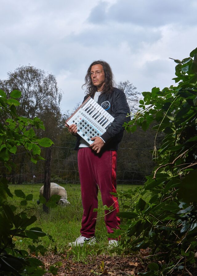 Electro-producer Legowelt in de natuur met een synthesizer onder zijn arm.