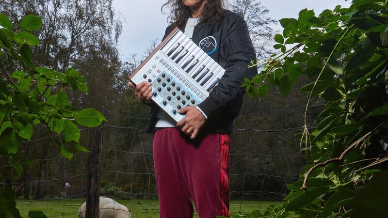Electro-producer Legowelt in de natuur met een synthesizer onder zijn arm.